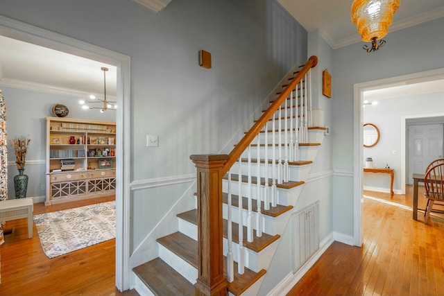 staircase featuring an inviting chandelier, hardwood / wood-style floors, and crown molding