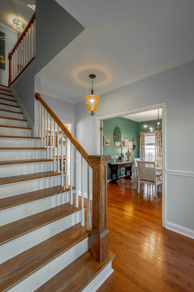 stairs featuring hardwood / wood-style floors, crown molding, and a notable chandelier