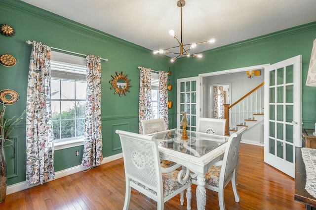 dining area with wood-type flooring, ornamental molding, a wealth of natural light, and a notable chandelier