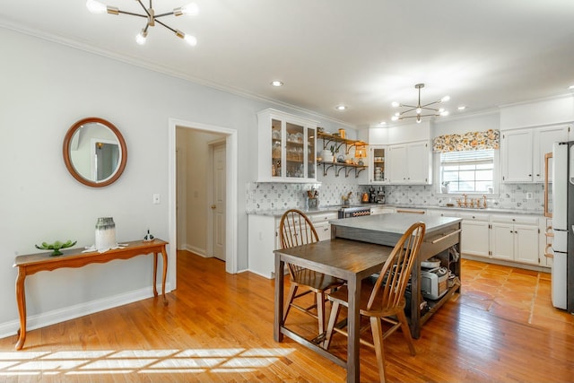 kitchen featuring light hardwood / wood-style flooring, an inviting chandelier, backsplash, white cabinetry, and ornamental molding