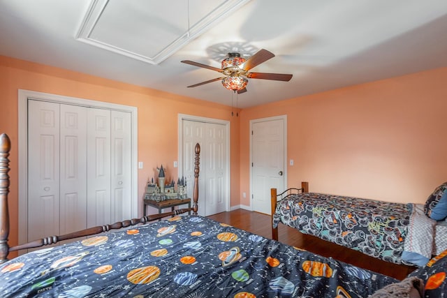 bedroom featuring two closets, wood-type flooring, and ceiling fan