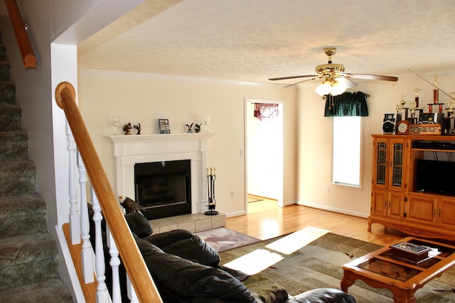 living room featuring light hardwood / wood-style flooring, ceiling fan, ornamental molding, a textured ceiling, and a tiled fireplace