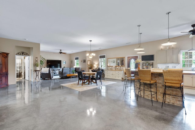 kitchen with pendant lighting, concrete flooring, a breakfast bar, and ceiling fan with notable chandelier