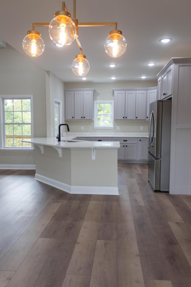 kitchen with pendant lighting, stainless steel refrigerator, sink, dark hardwood / wood-style flooring, and a kitchen island with sink