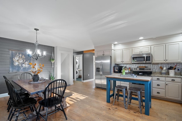 kitchen featuring wood walls, decorative light fixtures, appliances with stainless steel finishes, light hardwood / wood-style floors, and decorative backsplash