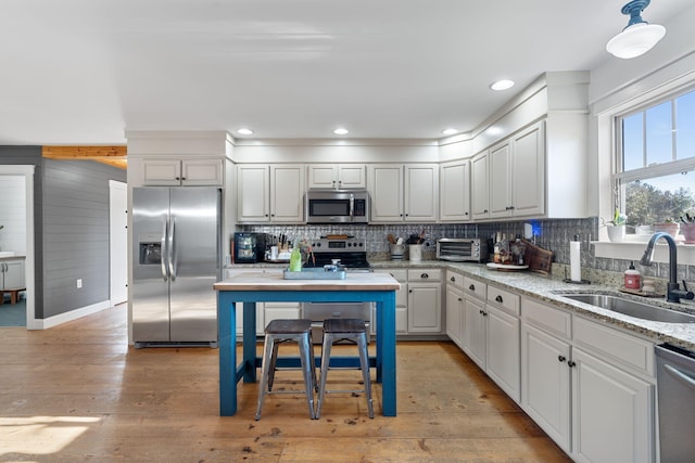 kitchen featuring sink, white cabinetry, light wood-type flooring, appliances with stainless steel finishes, and light stone countertops