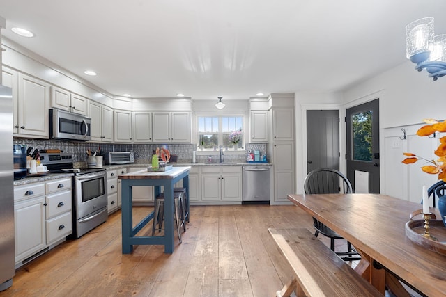 kitchen with sink, light stone counters, light wood-type flooring, stainless steel appliances, and backsplash