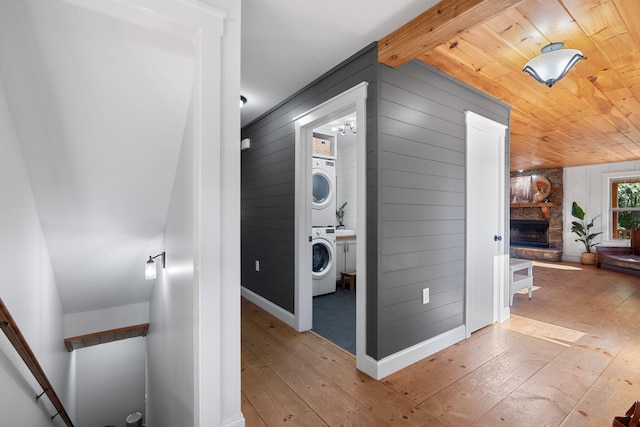 clothes washing area with wooden walls, stacked washer / drying machine, a stone fireplace, and light wood-type flooring