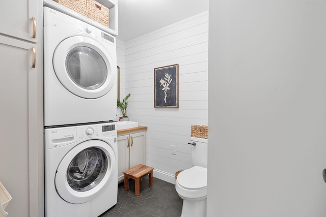 clothes washing area featuring stacked washer and dryer and dark tile patterned floors