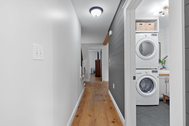 laundry area with hardwood / wood-style flooring, wooden walls, and stacked washer / dryer