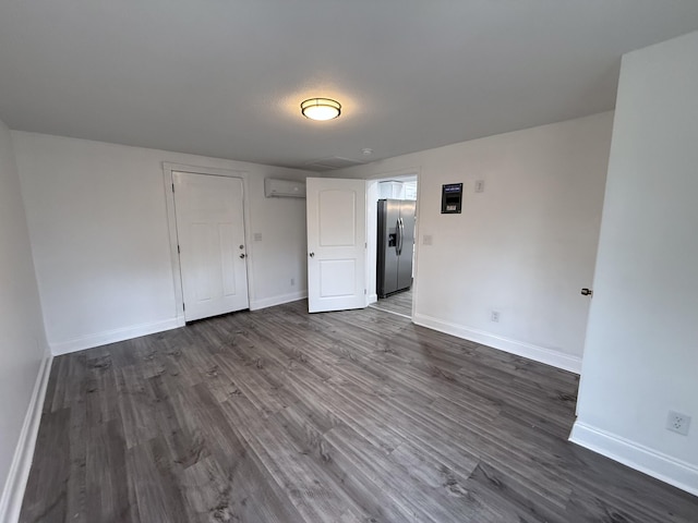 unfurnished bedroom with stainless steel fridge with ice dispenser, a wall mounted air conditioner, and dark wood-type flooring