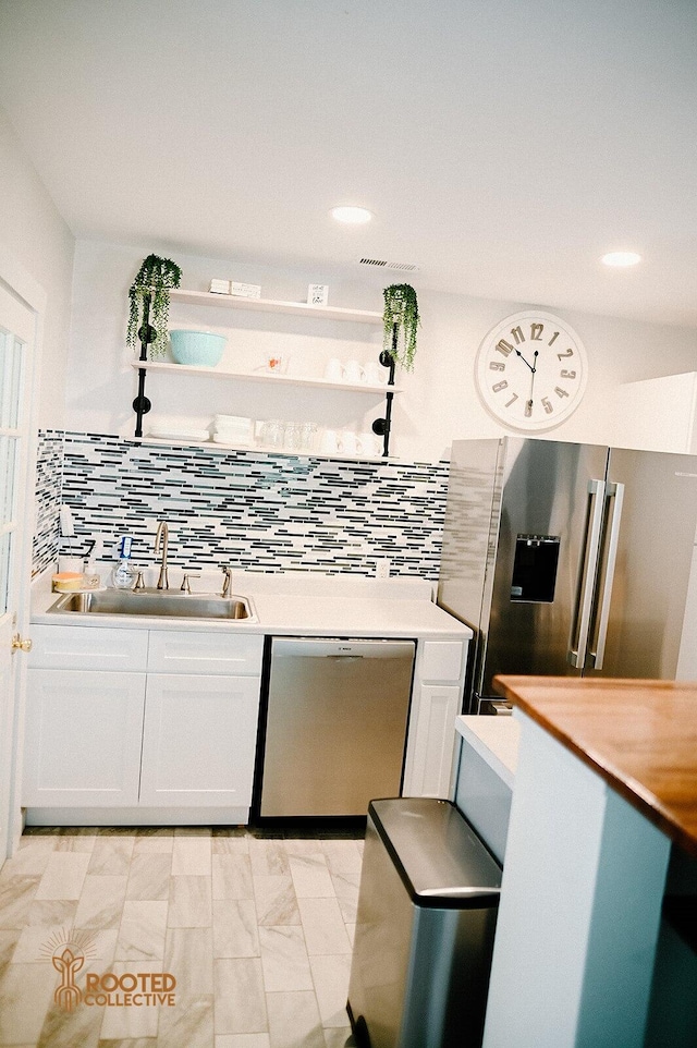 kitchen with light countertops, decorative backsplash, stainless steel appliances, white cabinetry, and a sink