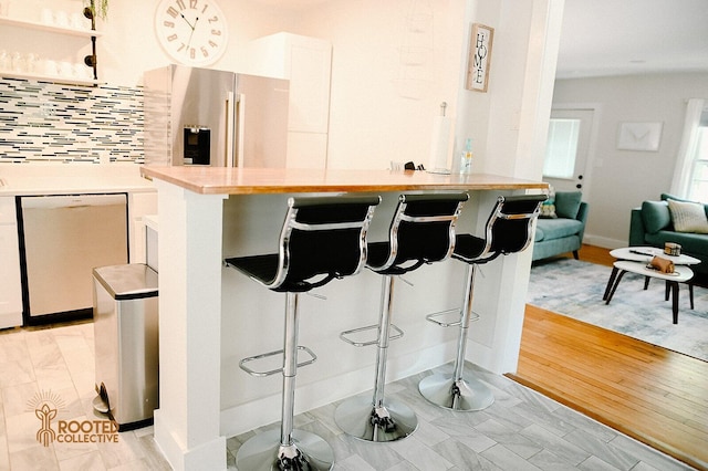 kitchen featuring a kitchen bar, backsplash, stainless steel appliances, white cabinets, and light countertops