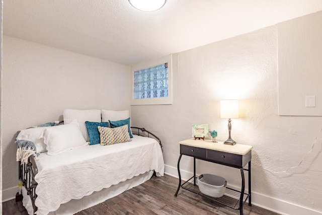 bedroom featuring baseboards, wood finished floors, and a textured wall