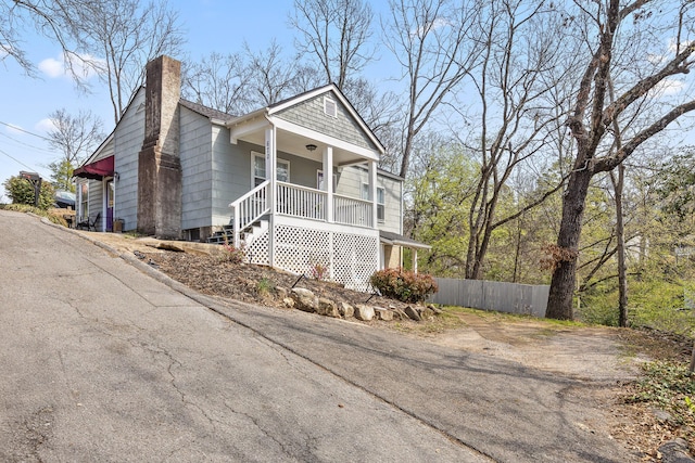 view of front of property with covered porch, driveway, a chimney, and fence