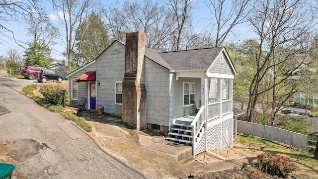 view of front of house featuring a shingled roof, a chimney, and fence