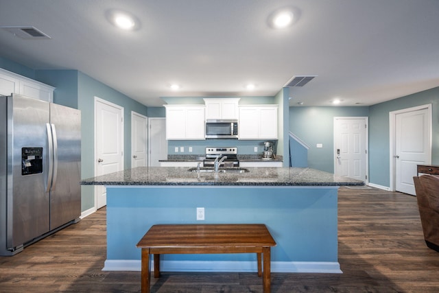 kitchen with stainless steel appliances, white cabinetry, dark stone countertops, and a center island with sink