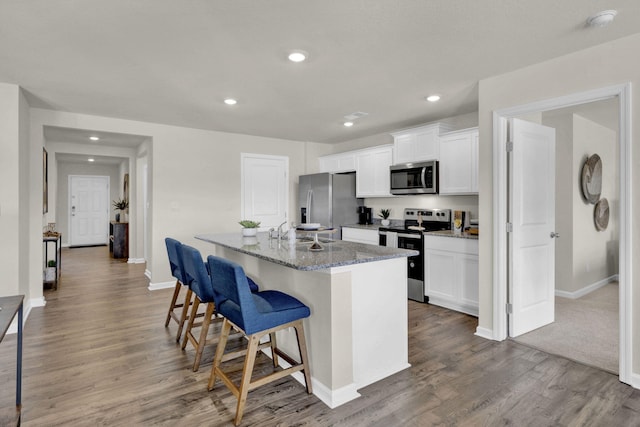 kitchen with white cabinetry, stainless steel appliances, a kitchen bar, and a center island with sink