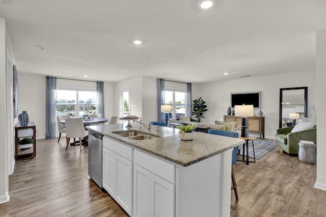 kitchen with sink, white cabinets, a kitchen island with sink, stainless steel dishwasher, and light stone counters