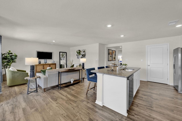 kitchen featuring sink, stone counters, appliances with stainless steel finishes, white cabinets, and a center island with sink