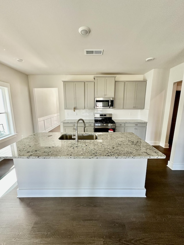 kitchen featuring visible vents, a kitchen island with sink, a sink, light stone counters, and stainless steel appliances