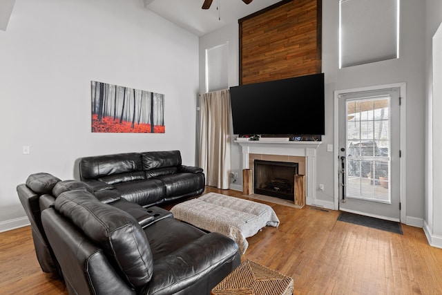 living room with a tile fireplace, high vaulted ceiling, ceiling fan, and light hardwood / wood-style floors