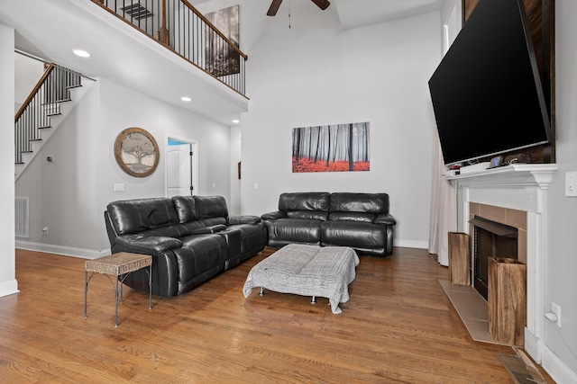 living room featuring hardwood / wood-style floors, a towering ceiling, a fireplace, and ceiling fan