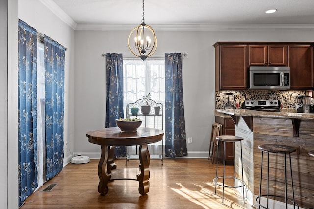 dining area featuring crown molding, a notable chandelier, and light wood-type flooring