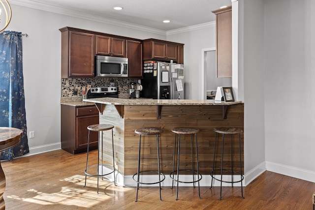 kitchen featuring appliances with stainless steel finishes, a kitchen breakfast bar, decorative backsplash, ornamental molding, and light hardwood / wood-style floors