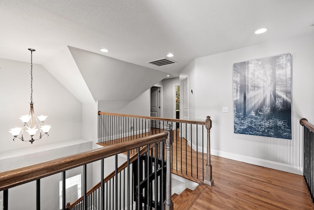 corridor featuring vaulted ceiling, hardwood / wood-style floors, a textured ceiling, and a notable chandelier