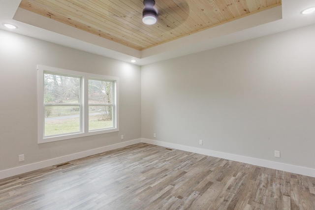 empty room with light hardwood / wood-style floors, wooden ceiling, and a raised ceiling