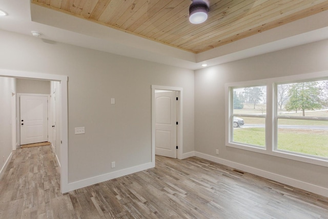 spare room featuring wood ceiling, a tray ceiling, and light wood-type flooring