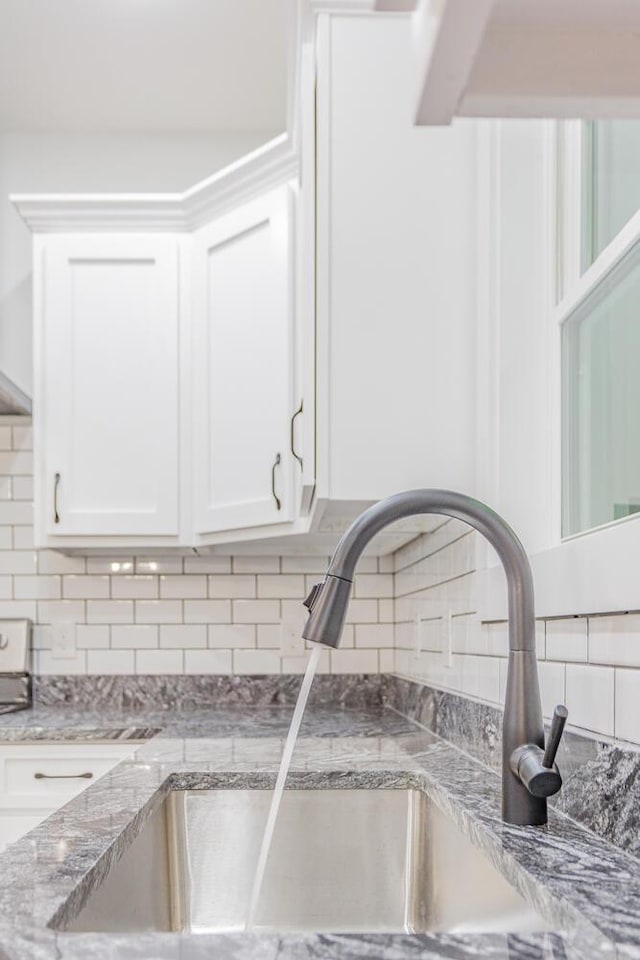 room details with white cabinetry, sink, backsplash, and light stone countertops