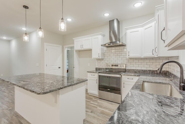 kitchen featuring wall chimney exhaust hood, sink, white cabinetry, stainless steel electric range oven, and decorative light fixtures