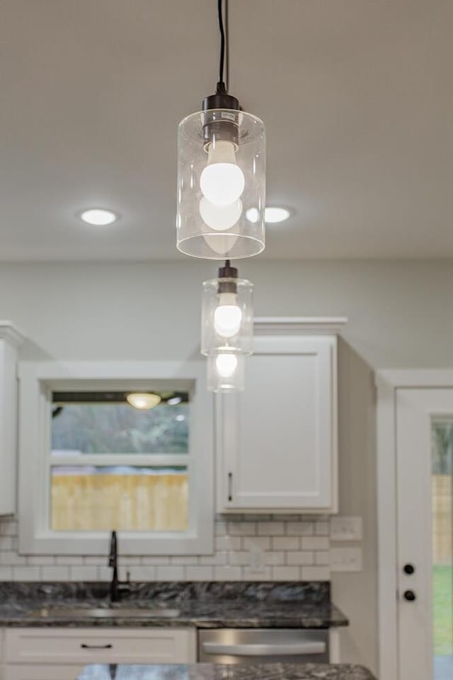 room details featuring sink, white cabinetry, hanging light fixtures, dark stone counters, and backsplash