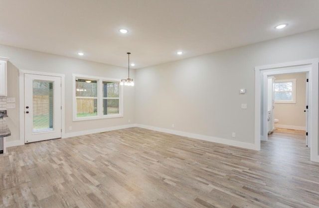 unfurnished living room featuring a chandelier and light wood-type flooring