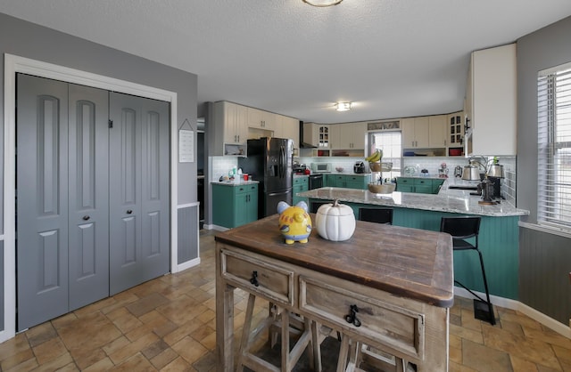 kitchen with wall chimney range hood, stainless steel fridge, tasteful backsplash, cream cabinets, and kitchen peninsula