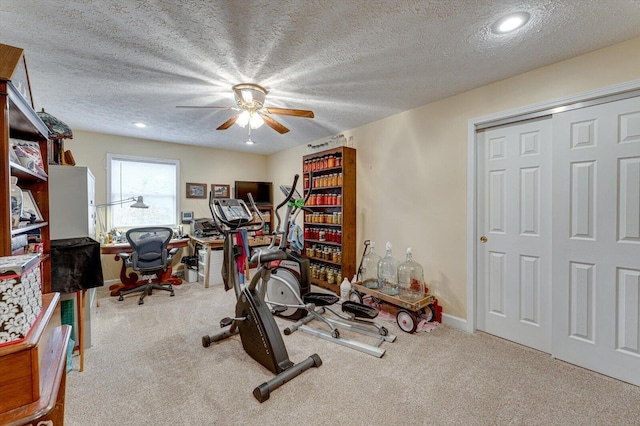 exercise area featuring ceiling fan, light colored carpet, and a textured ceiling