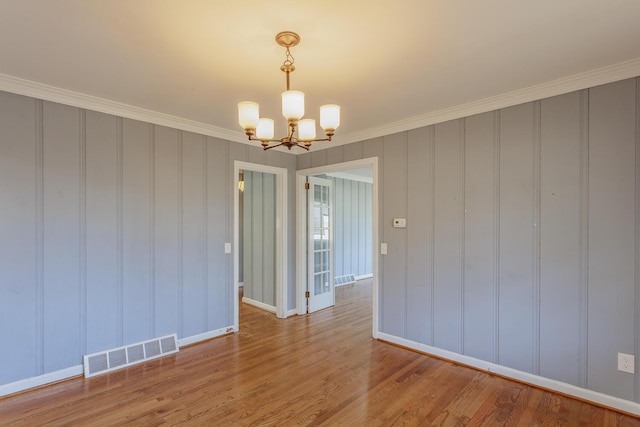 empty room featuring an inviting chandelier, crown molding, and light hardwood / wood-style floors