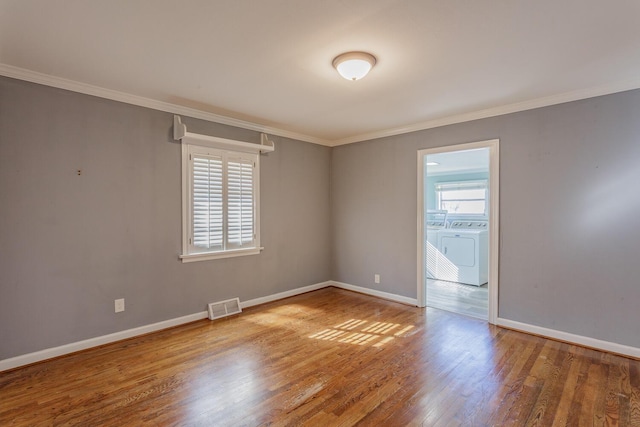 empty room with hardwood / wood-style flooring, ornamental molding, and washer and dryer