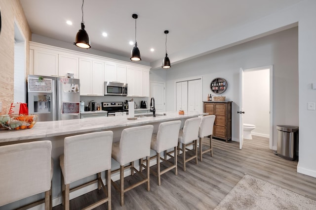 kitchen featuring a breakfast bar, hanging light fixtures, stainless steel appliances, light stone countertops, and white cabinets