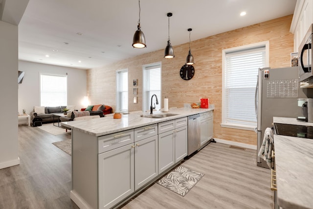 kitchen featuring stainless steel appliances, sink, pendant lighting, and light stone counters