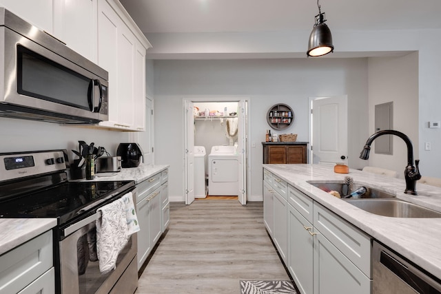 kitchen with sink, hanging light fixtures, stainless steel appliances, washer and dryer, and white cabinets