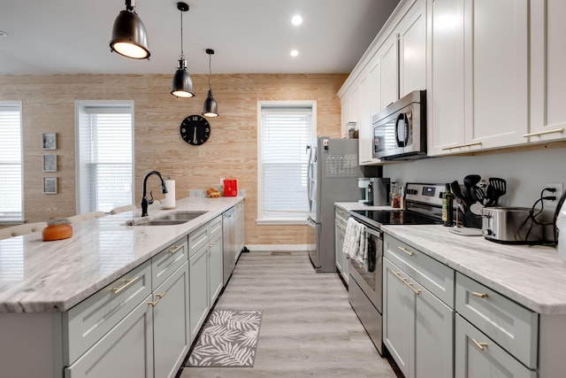 kitchen with light stone counters, appliances with stainless steel finishes, sink, and hanging light fixtures