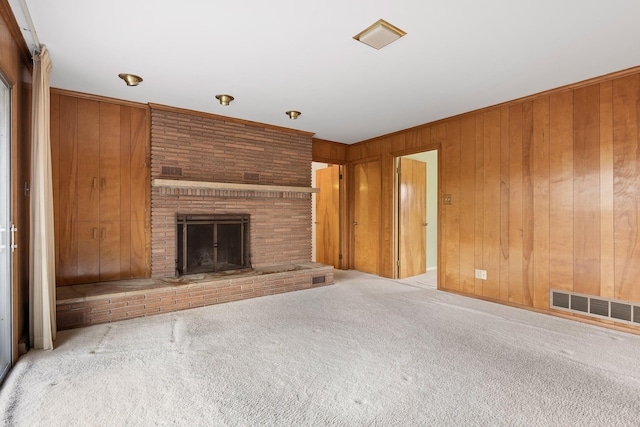 unfurnished living room with light colored carpet, ornamental molding, a brick fireplace, and wood walls