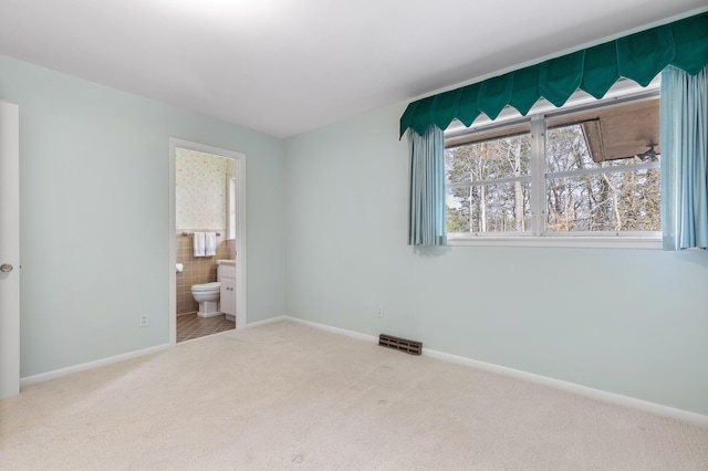 unfurnished bedroom featuring connected bathroom, carpet flooring, and tile walls