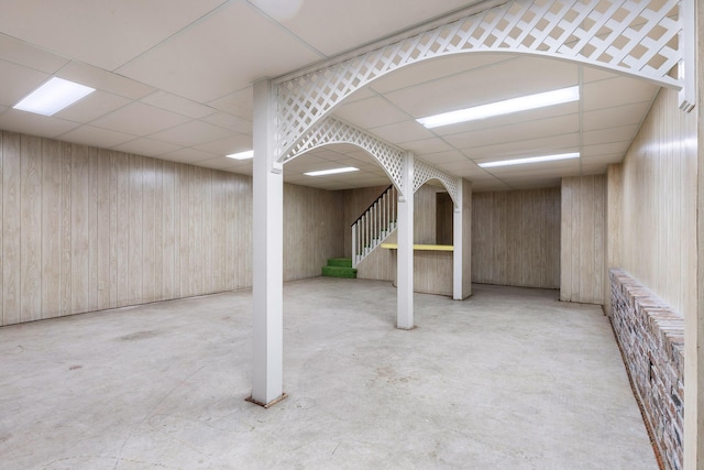 basement featuring a paneled ceiling and wood walls