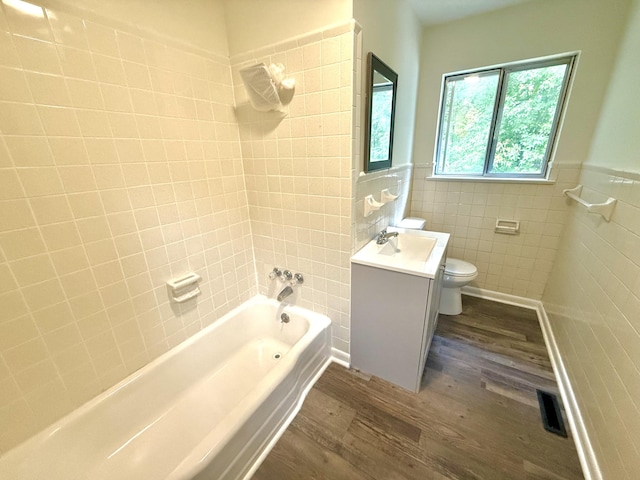 full bathroom with toilet, tiled shower / bath, tile walls, vanity, and hardwood / wood-style flooring