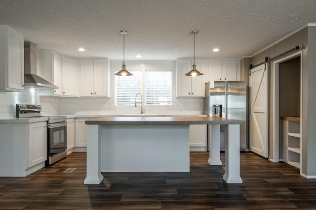 kitchen with white cabinetry, decorative light fixtures, stainless steel appliances, a barn door, and wall chimney range hood