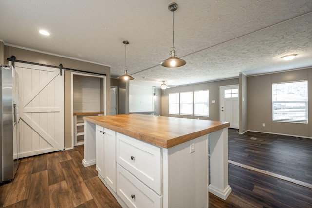 kitchen featuring butcher block counters, a center island, white cabinets, decorative light fixtures, and a barn door